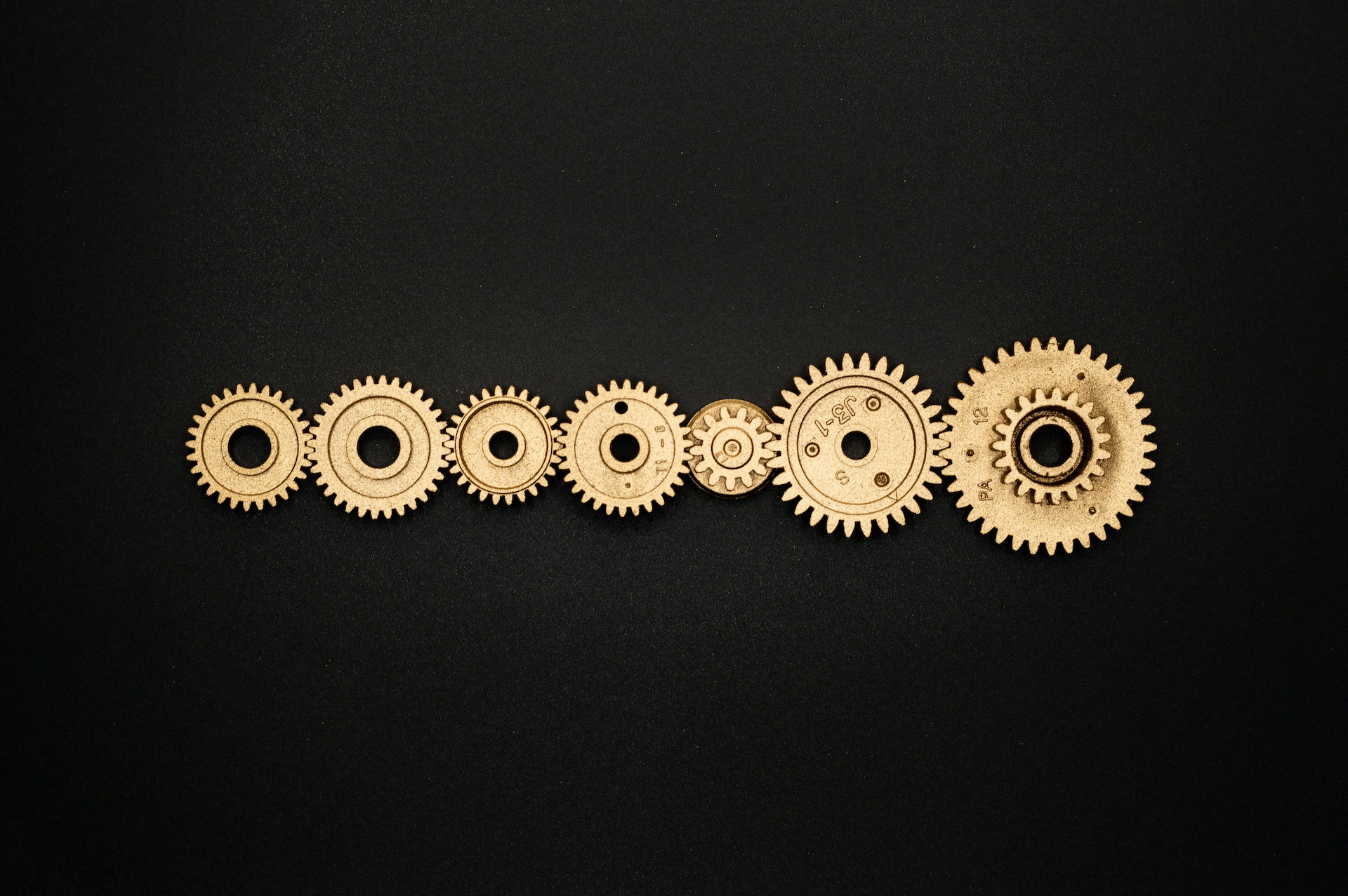 7 golden gears of different sizes, in front of a black background